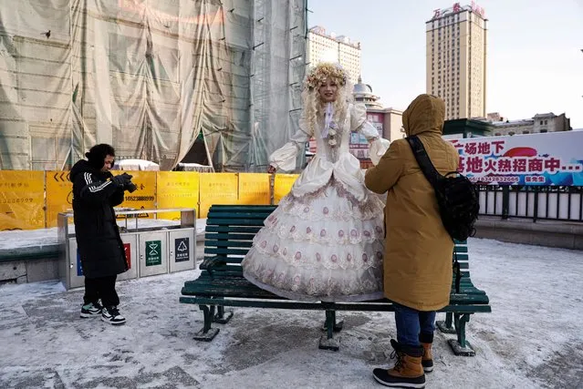 A woman wearing a costume stands on a bench as she poses for pictures during a photo shooting session, near the Saint Sophia Cathedral in Harbin, Heilongjiang province, China on January 5, 2024. (Photo by Tingshu Wang/Reuters)