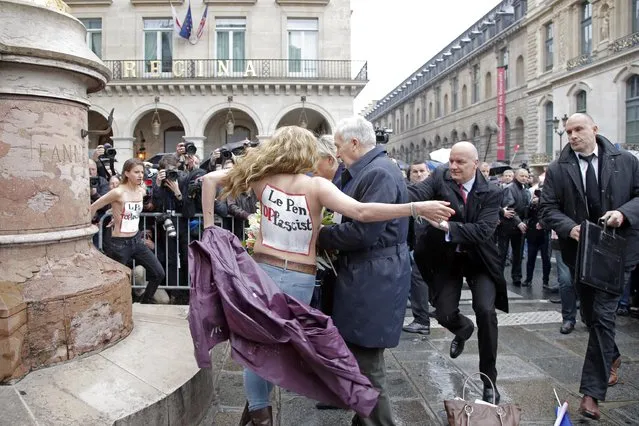 FEMEN activists with Le Pen Top Fascist painted on their bodies appear as France's far-right National Front president Marine Le Pen places a wreath at Joan of Arc Statue during its annual May Day march, in Paris, France, Friday, May 1, 2015. France's far-right National Front is holding its annual May Day march, but for the first time the party's founder Jean-Marie Le Pen – on the outs with his daughter who presides over the party – is not taking a seat at the tribune. (Photo by Francois Mori/AP Photo)