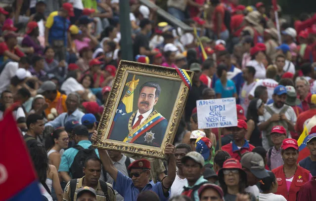 A government supporter holds up a framed image of President Nicolas Maduro during an anti-imperialist rally in Caracas, Venezuela, Saturday, March 30, 2019. Venezuelan opposition leader Juan Guaido took his campaign for change to one of the country's most populous states on Saturday, while supporters of the man he is trying to oust, President Nicolas Maduro, held a rival demonstration in the capital after another nationwide blackout. (Photo by Ariana Cubillos/AP Photo)