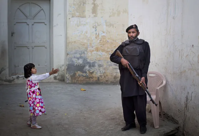 In this November 15, 2012 photo, a young girl reaches out to greet a Pakistani policeman securing the road outside Kainat Riaz's home in Mingora, Swat Valley, Pakistan. (Photo by Anja Niedringhaus/AP Photo)