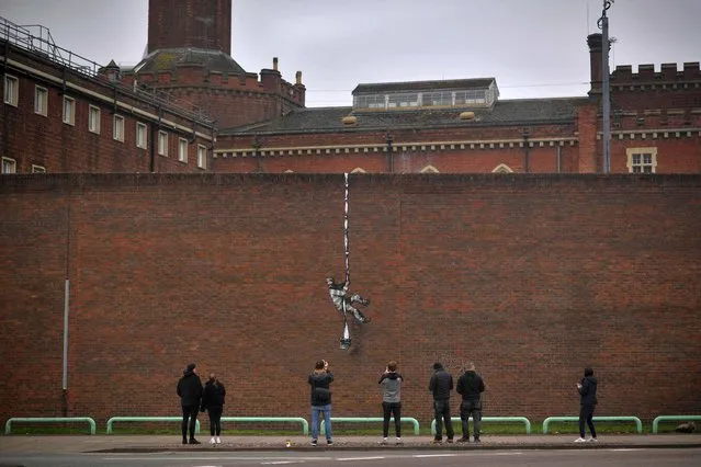 Members of the public pause to look at an artwork bearing the hallmarks of street artist Banksy on the side of Reading Prison in Reading, west of London, on March 2, 2021. The picture shows a prisoner, possibly resembling famous inmate Oscar Wilde, escaping on a rope made of bedsheets tied to a typewriter. The work not yet been claimed by Banksy. (Photo by Ben Stansall/AFP Photo)