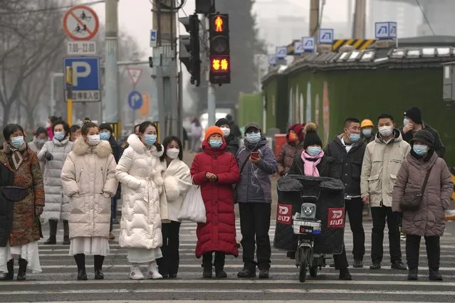 Pedestrians wearing face masks to help protect from the coronavirus wait to cross an intersection in the Central Business District of Beijing, Monday, January 24, 2022. A fresh outbreak in Beijing has prompted authorities to test millions and impose new measures two weeks ahead of the opening of the Winter Olympics, even as Chinese officials on Monday lifted a monthlong lockdown on the northern city of Xi'an and its 13 million residents. (Photo by Andy Wong/AP Photo)