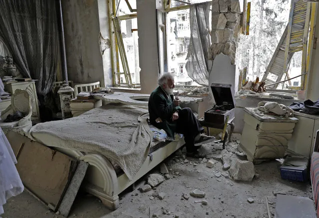 Mohammad Mohiedine Anis, 70, smokes his pipe as he sits in his destroyed bedroom listening to music on his vinyl player in Aleppo' s formerly rebel- held al- Shaar neighbourhood. (Photo by Joseph Eid/AFP Photo)