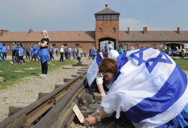 A girl places a plaque on the rail tracks in the former German Nazi Death Camp Auschwitz-Birkenau during the yearly March of the Living, in Brzezinka, Poland, Thursday, May 5, 2016. Thousands of people from around the world have paid homage to the victims of the Holocaust with a somber march from the barracks of Auschwitz to nearby Birkenau. (Photo by Alik Keplicz/AP Photo)