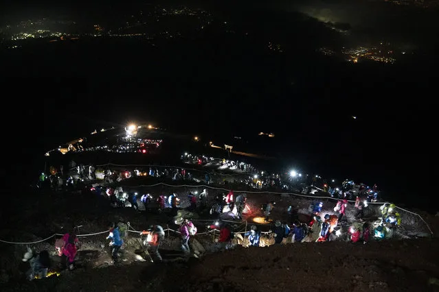 Hundreds of climbers wearing headlamps form a long line as they climb to the summit of Mount Fuji to watch the sunrise, Saturday, August 3, 2019, in Japan. It takes an average hiker five to six hours to reach the summit. Most spend the night in simple mountain huts and start the final ascent in darkness. (Photo by Jae C. Hong/AP Photo)