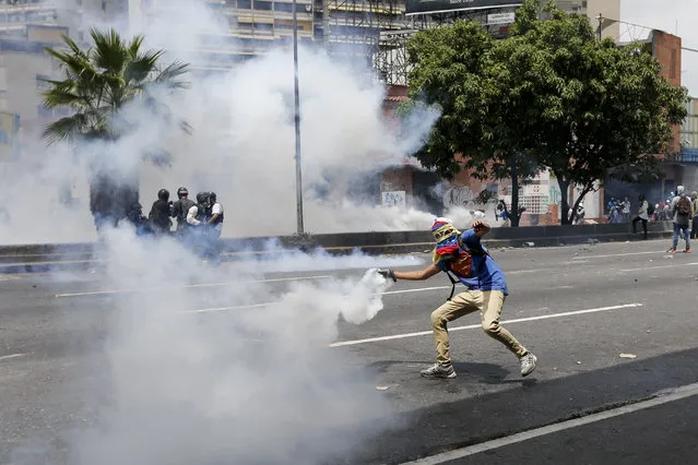 A demonstrator returns a canister of tear gas towards security forces during anti-government protests in Caracas, Venezuela, Wednesday, April 19, 2017. (Photo by Ariana Cubillos/AP Photo)
