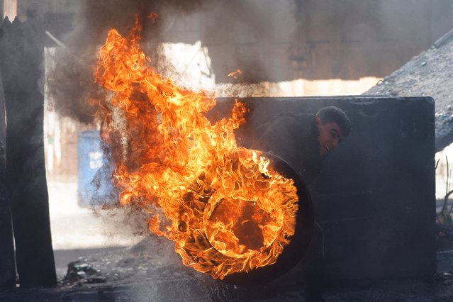 A Palestinian pushes a burning tyre during clashes in Hebron, in the Israeli-occupied West Bank, January 21, 2022. (Photo by Mussa Qawasma/Reuters)