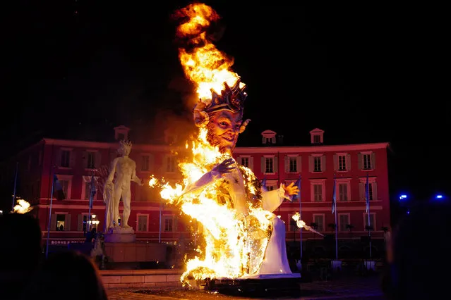 Spectators look at a giant figure of a king burning during the 137th Nice Carnival parade in Nice, southeastern France, on February 26, 2022. The Carnival takes place until February 27, 2022 on the theme “King of animals”. (Photo by Valery Hache/AFP Photo)