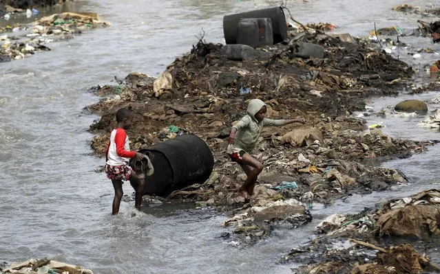 Boys wade through the Nairobi river past empty barrels of alcohol recovered from an illegal micro-brewery for distilling traditional liquor, locally known as “chang'aa”, within Mathare valley slums in Kenya's capital Nairobi, July 11, 2015. According to local media, Kenyans have been advised by President Uhuru Kenyatta to refrain from destroying property where illict alcohol is found, in light of the increase in operations against illegally brewed alcohol which Kenyatta said is necessary in order for youths to be part of national development. (Photo by Thomas Mukoya/Reuters)