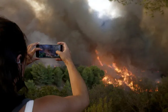 A woman takes pictures the flames during a wildfire in the area of Varybobi, northeastern suburb of Athens, Greece, 03 August 2021. The wildfire that broke out in a forest in the Varybobi area on August 3rd spread quickly due to the dry conditions, despite the lack of strong winds and the efforts of fire-fighting forces to contain it quickly. There are 350 fire-fighters with 70 vehicles, 10 teams of fire fighters on foot and five helicopters and five aircrafts, including a Beriev 200, deployed to put out the fire. The police have stopped the movement of vehicles on the Tatoiou Road between Kymis Avenue and Erithrea Road, on Erithrea Road between the Varybobi bridge and on Tatoiou from Parnithos Road (Ippokratios Politia). (Photo by Yiannis Kolesidis/EPA/EFE/Rex Features/Shutterstock)