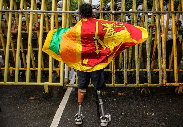 A retired soldier carrying a Sri Lanka's national flag stands next to a police barricade during a demonstration against the economic crisis near the parliament building in Colombo on April 8, 2022. Cash-strapped Sri Lanka's central bank hiked interest rates by a record 700 basis points April 8, as police fired tear gas at hundreds of students protesting about the economic crisis. (Photo by AFP Photo/Stringer)