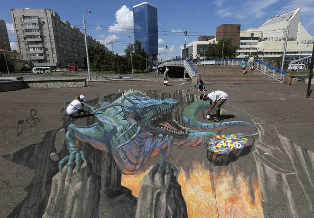 U.S. artist Tracy Lee Stum (L) and her assistants work on the “Singing Dragon” interactive 3D street painting as they take part in the 4th Krasnoyarsk International Music Festival of the Asian-Pacific region in central Krasnoyarsk, Siberia, June 27, 2014. More than 600 artists, dancers and actors representing 29 countries from all over the world will take part in more than 100 concerts and exhibitions during a one-week-long festival in the centre of Siberia, according to organizers. (Photo by Ilya Naymushin/Reuters)