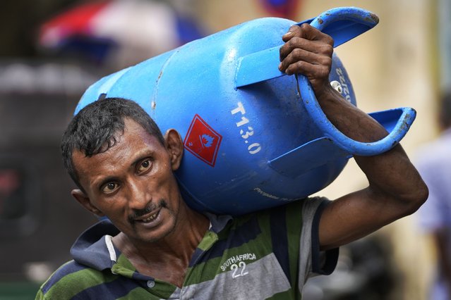 A man carries a cooking gas cylinder purchased from a distribution centre in Colombo, Sri Lanka, Saturday, May 14, 2022. Sri Lankans have been forced to wait in long lines to purchase scarce imported essentials such as medicines, fuel, cooking gas and food because of a severe foreign currency shortage. (Photo by Eranga Jayawardena/AP Photo)