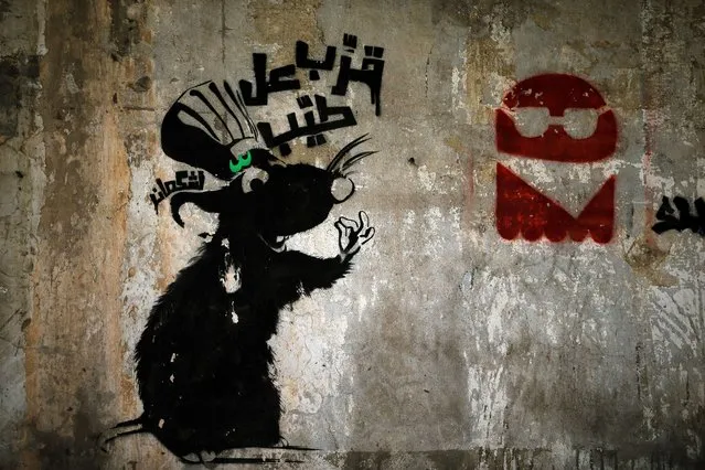 Graffiti  showing a picture of a rat and reading in Arabic: “Come and taste the goodies” is seen sprayed above piles of rubbish in Beirut on July 28, 2015, as the Lebanese capital and the surrounding region continue to live in a trash crisis after residents living near the country's largest landfill shut it down. Activists and residents of Naameh and surrounding villages are blocking a road leading to the Naameh landfill, preventing trash deliveries to the site. (Photo by Joseph Eid/AFP Photo)
