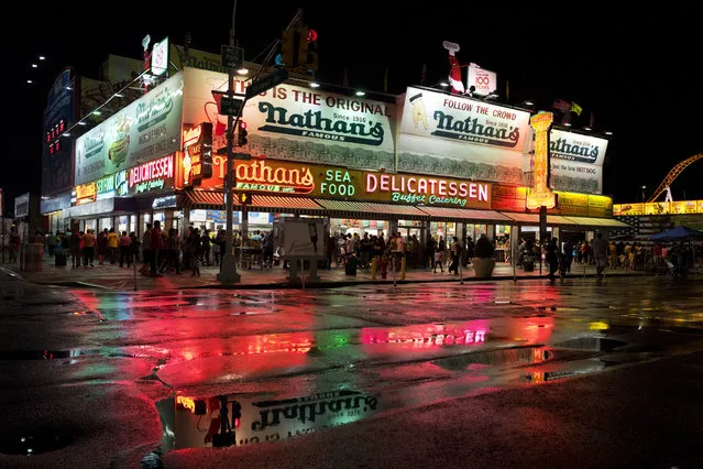 In this August 12, 2017 photo, Nathan's Famous hot dog restaurant is reflected in a rain dampened Coney Island street in the Brooklyn borough of New York. (Photo by Mark Lennihan/AP Photo)