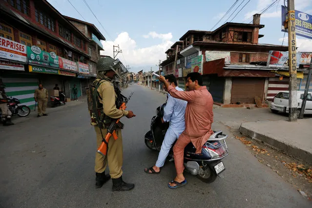An Indian policeman stops men on a scooter during a curfew in Srinagar July 12, 2016. (Photo by Danish Ismail/Reuters)