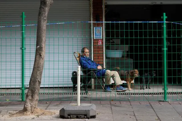 A man sits with three dogs behind a barrier at a sealed area following the coronavirus outbreak, in Shanghai, China on October 11, 2022. Shanghai, a city of 25 million people, reported 28 local cases for Oct. 10, the fourth day of double-digit increases. (Photo by Aly Song/Reuters)