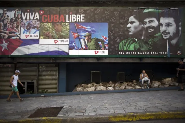 Waiter Denis Sosa, 33, (R), uses his mobile phone to connect to the internet under an outdoor sign with images of Cuban late rebel revolutionary Camilo Cienfuegos (C), revolutionary hero Ernesto “Che” Guevara (R) and co-founder of the first Communist Party of Cuba, Julio Antonio Mella, with messages reading “Long live free Cuba”, Havana, September 18, 2015. (Photo by Alexandre Meneghini/Reuters)