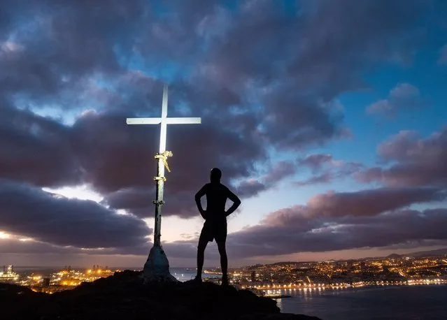 A trail runner's head torch illuminates a mountain summit cross in pre dawn light, with Las Palmas city in distance, Canary Islands, Spain on November 29, 2022. (Photo by Alan Dawson/Alamy Live News)
