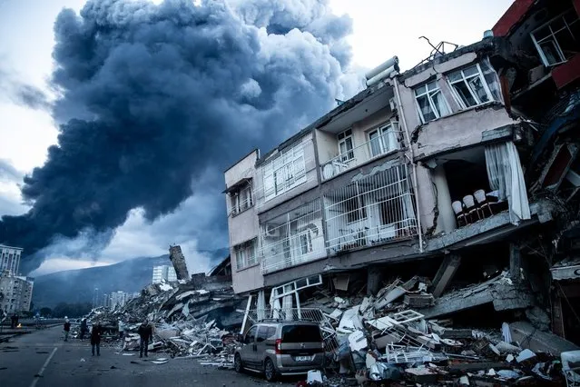 Smoke billows from Iskenderun Port fire as people walk past collapsed buildings on February 07, 2023 in Iskenderun, Turkey. A 7.8-magnitude earthquake hit near Gaziantep, Turkey, in the early hours of Monday, followed by another 7.5-magnitude tremor just after midday. The quakes caused widespread destruction in southern Turkey and northern Syria and were felt in nearby countries. (Photo by Burak Kara/Getty Images)