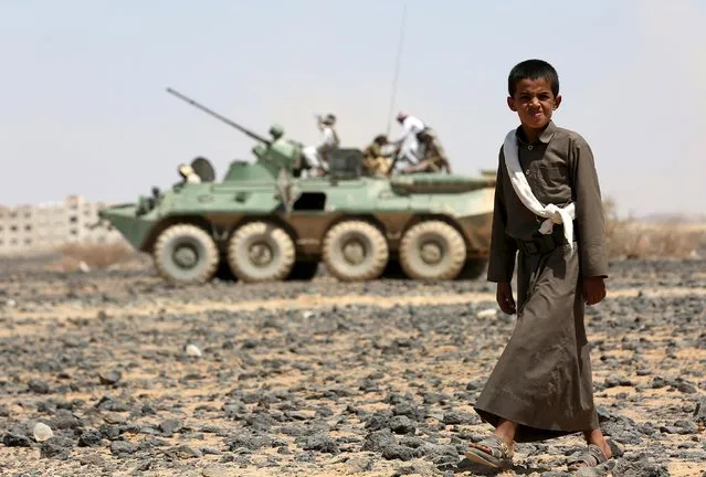 A boy walks in front of fighters of the Popular Resistance Committees riding on an armoured vehicle during a ceremony where they formally take over territory that the government had managed to recover from Houthi militants, in the central province of Marib October 11, 2015. (Photo by Reuters/Stringer)