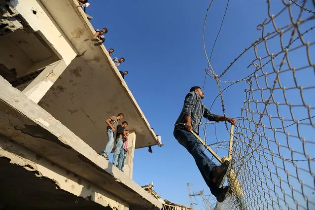 A Palestinian man climbs a fence as he waits for the return of his relatives from Saudi Arabia after performing the annual haj pilgrimage, outside Rafah border crossing with Egypt, in the southern Gaza Strip October 8, 2015. (Photo by Ibraheem Abu Mustafa/Reuters)