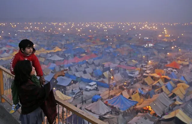 An Indian woman shows her child makeshift tents of Hindu devotees at the confluence of the rivers Ganges, Yamuna and the mythical Saraswati, on the eve of “Mauni Amavasya” or new moon day, considered the most auspicious date of bathing during the annual month long Hindu religious fair “Magh Mela” in Allahabad, India, Monday, January 19, 2015. (Photo by Rajesh Kumar Singh/AP Photo)