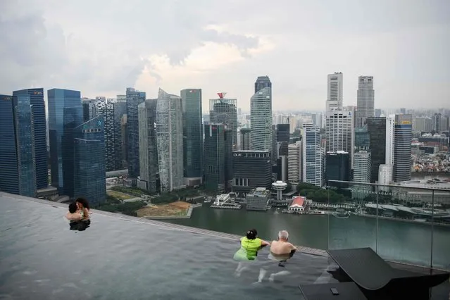 This photo taken on June 13, 2018 shows a couple (L) embracing as another couple (R) looks at the view from the rooftop pool of the Marina Bay Sands resort hotel, which overlooks the financial district skyline of Singapore. (Photo by Anthony Wallace/AFP Photo)