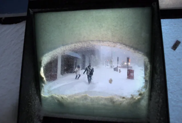 Jennifer Rice and Mike Femia battle wind-driven snow as they make their way to their jobs at a pharmaceutical lab, as seen through a window, Tuesday, January 27, 2015, in downtown Portland, Maine.  Forecasters with the National Weather Service in Gray have said that much of southern Maine will see 12 to 18 inches of snow, while small bands of intense snowfall will increase those totals in localized areas. (Photo by Robert F. Bukaty/AP Photo)