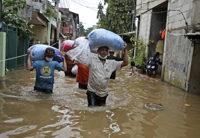 Indonesian men carry their belongings as they wade through the water at a flooded neighborhood following heavy rains in Jakarta, Indonesia, Friday, February 19, 2021. Heavy downpours combined with poor city sewage planning often causes heavy flooding in parts of greater Jakarta. (Photo by Dita Alangkara/AP Photo)