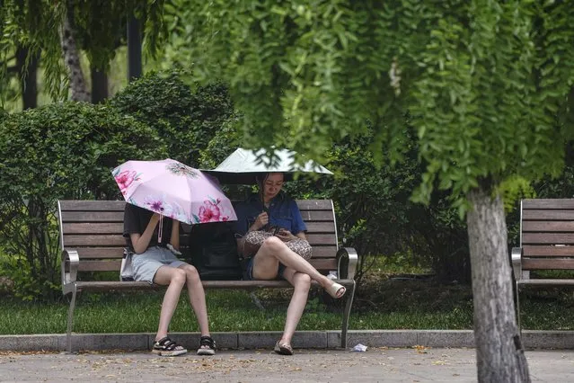 Residents carry umbrellas to shield from the sun as they take rest on a bench on a hot day in Beijing, Monday, July 3, 2023. Heavy flooding has displaced thousands of people around China as the capital had a brief respite from sweltering heat. (Photo by Andy Wong/AP Photo)