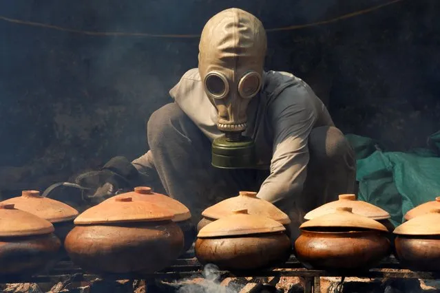 Bui Van Cuong wears a gas mask as he braises black carp in claypots with longan firewood to serve as a traditional Vietnamese dish for Lunar New Year celebrations in Ha Nam province, Vietnam on February 5, 2021. (Photo by Kham via Reuters)