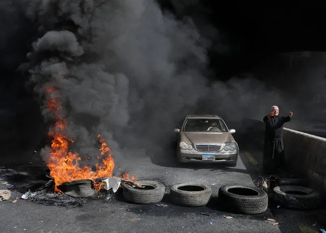 A Maronite Christian priest pleads anti-government protesters to let him pass with his vehicle as he stands next to burning tires at a make-shift roadblock in Zouk Mosbeh north of Lebanon's capital Beirut, on March 8, 2021 as they protest against the deteriorating value of the local currency and dire economic and social conditions. (Photo by Joseph Eid/AFP Photo)