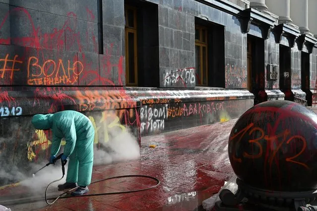 A cleaning company employee washes away inscriptions left by protesters on the Ukrainian President Volodymyr Zelensky's office during recent rally to demand the release of Serhiy Sternenko, a civil activist and former leader of the far-right group Right Sector, who was sentenced by an Odessa court to seven years and three months in prison, in central Kiev on March 23, 2021. (Photo by Sergei Supinsky/AFP Photo)