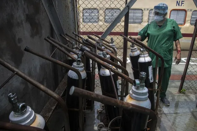 A health worker checks oxygen cylinders stored next to a train prepared as COVID-19 care centre in the wake of spike in the number of positive coronavirus cases, at a railway station in Gauhati, India, Thursday, May 6, 2021. Infections in India hit another grim daily record on Thursday as demand for medical oxygen jumped seven-fold and the government denied reports that it was slow in distributing life-saving supplies from abroad. (Photo by Anupam Nath/AP Photo)