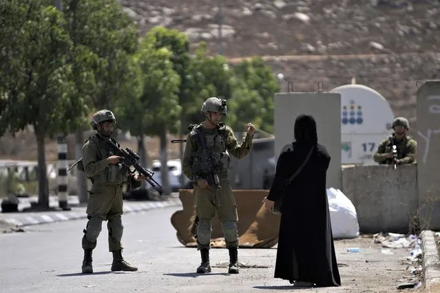 Israeli soldiers speak to a Palestinian woman near the site of an alleged car-ramming attack near Beit Hagai, a Jewish settlement in the hills south of the large Palestinian city of Hebron, Wednesday, August 30, 2023. The Israeli military said security forces shot the Palestinian driver as he accelerated toward a military post. A soldier struck by the car was evacuated to a nearby hospital for treatment. There was no immediate word on the condition of the suspected Palestinian assailant. (Photo by Mahmoud Illean/AP Photo)