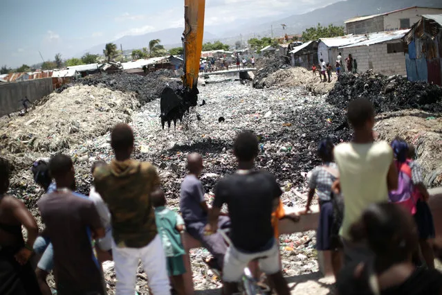 People watch as an excavator takes garbage out of a river in Cite Soleil, Port-au-Prince, Haiti on May 21, 2018. (Photo by Andres Martinez Casares/Reuters)