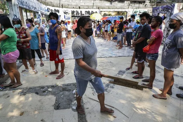 A woman holds a piece of wood as she asks other residents to maintain social distancing as they queue for free food at a “community pantry” which has popped up across the capital to help people cope during the government lockdown to curb the spread of the coronavirus in Quezon city, Philippines on Thursday, April 29, 2021. The Philippines is extending an already monthlong lockdown by two weeks as the country's worst coronavirus infection spike starts to ease but remains alarming. (Photo by Aaron Favila/AP Photo)