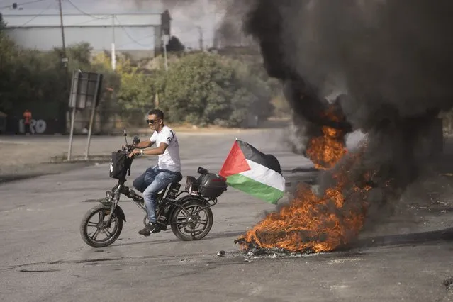 A protester rides his bicycle through burning tires during clashes with the Israeli border police following a demonstration in solidarity with the Gaza Strip, in the West Bank city of Ramallah, Friday, October 20, 2023. (Photo by Nasser Nasser/AP Photo)