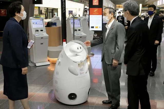 Japanese Prime Minister Yoshihide Suga, center, stands by a remotely-controlled guide robot at Haneda international airport in Tokyo, Monday, June 28, 2021. Suga inspected antigen testing for arrivals and vowed to ensure appropriate border controls as growing numbers of Olympic and Paralympic participants enter Japan ahead of the July 23 opening of the games (Photo by Kyodo News via AP Photo)