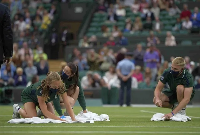 The court is dried with the help of towels as rain delays the men's singles fourth round match between Germany's Alexander Zverev and Canada's Felix Auger-Aliassime on day seven of the Wimbledon Tennis Championships in London, Monday, July 5, 2021. (Photo by Alastair Grant/AP Photo)