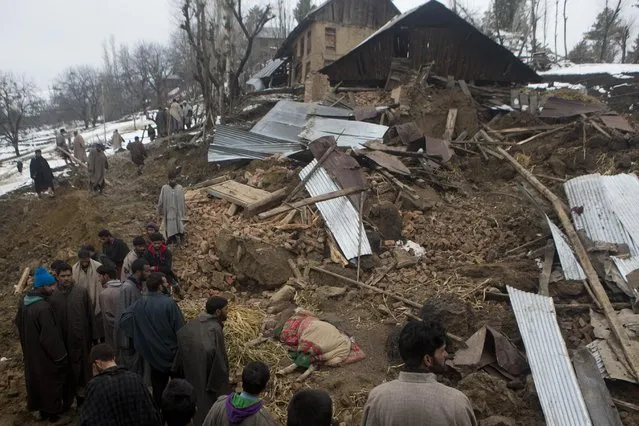 Kashmiri villagers stand near an injured horse close to a damaged house following landslides due to heavy rainfall in the village of Laden some 45 Kilometers (28 miles) west of Srinagar, Indian-controlled Kashmir, Monday, March 30, 2015. (Photo by Dar Yasin/AP Photo)