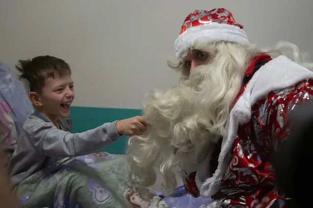 A boy pulls the beard of a Russian emergency rescue worker dressed as Ded Moroz (Santa Claus, or Father Frost ) after scaling the wall at a children hospital in Moscow, Russia, Thursday, December 27, 2018. The action marked the approach of the New Year. (Photo by Alexander Zemlianichenko/AP Photo)