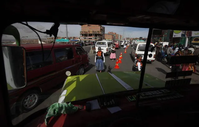 In this Dec. 3, 2013 photo, Aymara women traffic cops, seen through the windshield of a bus, direct traffic on the streets of El Alto, Bolivia. (Photo by Juan Karita/AP Photo)