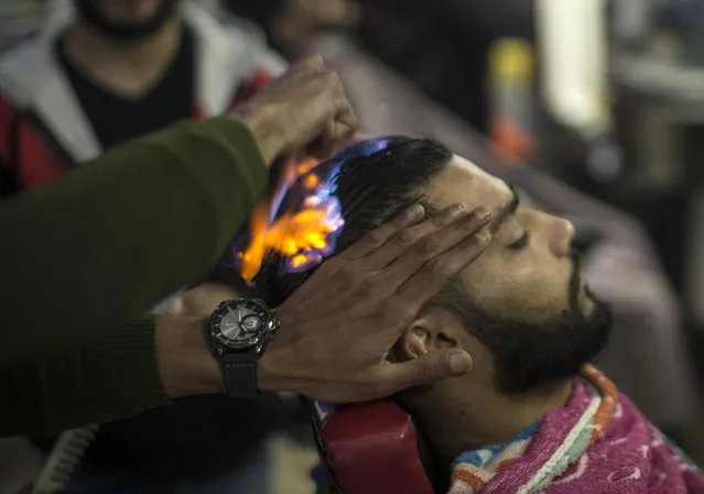 A client sits in a hair salon as barber Ramadan Edwan performs a technique that utilises fire to straighten his hair, in the Rafah refugee camp, in the southern Gaza Strip on February 1, 2017. (Photo by Mahmud Hams/AFP Photo)