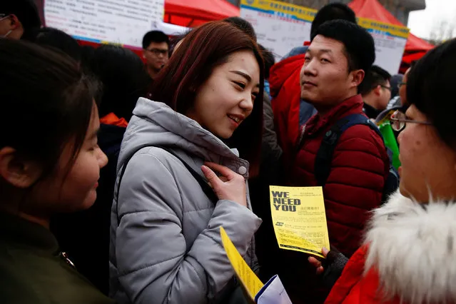 A recruiter hands out a company flyer to job seekers at an open air employment fair for college  graduates and the general public in the centre of Shijiazhuang, Hebei province, China, February 6, 2017. (Photo by Thomas Peter/Reuters)
