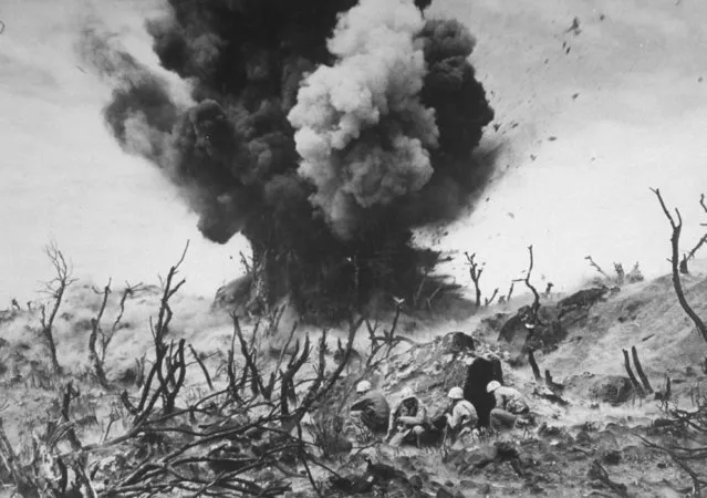 US Marines crouching behind hillside rock cover, blowing up cave connected to Japanese blockhouse in WWII action on Iwo Jima, Volcano Islands, 1945. (Photo by W. Eugene Smith/The LIFE Picture Collection/Getty Images)