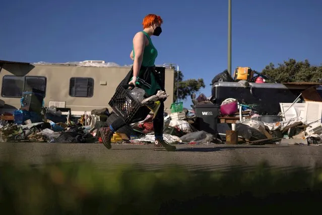 A volunteer helps to clean up belongings at an encampment of homeless people near the Nimitz Freeway in Oakland after the city issued an order to remove and clean up the area where between 30 to 40 people live in cars, RVS, tents, and other makeshift structures, April 2, 2024. (Photo by Carlos Barria/Reuters)