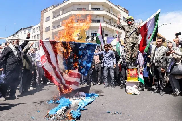Iranians burn US and Israeli flags during the annual Quds (Jerusalem) Day commemorations and the funeral of seven Revolutionary Guard Corps members killed in a strike on the country's consular annex in Damascus, which Tehran blamed on Israel, on April 5, 2024 in Tehran. The Guards, including two generals, were killed in the air strike on April 1, which levelled the Iranian embassy's consular annex in Damascus. The funeral ceremony coincides with the annual Quds (Jerusalem) Day commemorations, when Iran and its allies stage marches in support of the Palestinians. (Photo by Atta Kenare/AFP Photo)