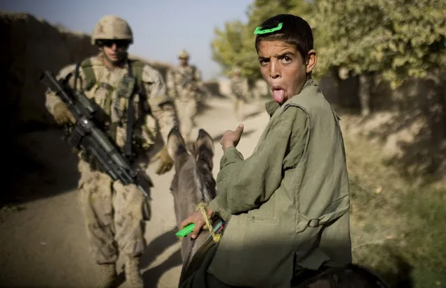 In this photo taken Saturday, September 11, 2010, an Afghan boy on a donkey reacts as Canadian soldiers with the 1st RCR Battle Group, The Royal Canadian Regiment, patrol in Salavat, southwest of Kandahar, Afghanistan. Minutes later the soldiers were attacked by grenades while leaving the village. (Photo by Anja Niedringhaus/AP Photo)